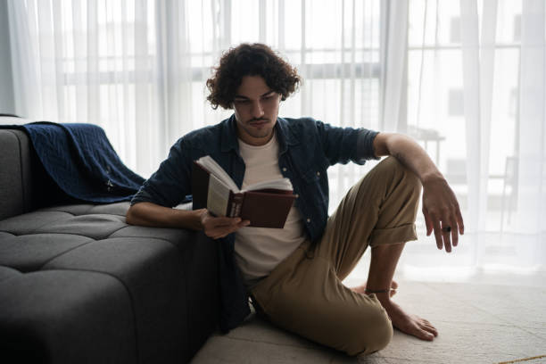 istock Young man sitting on the ground and reading at home 1327180979