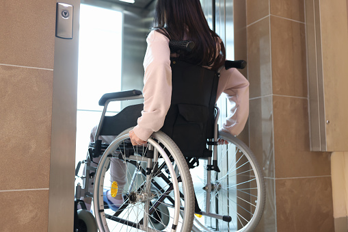 Disabled woman in wheelchair entering elevator back view. Comfortable living conditions for people with disabilities concept