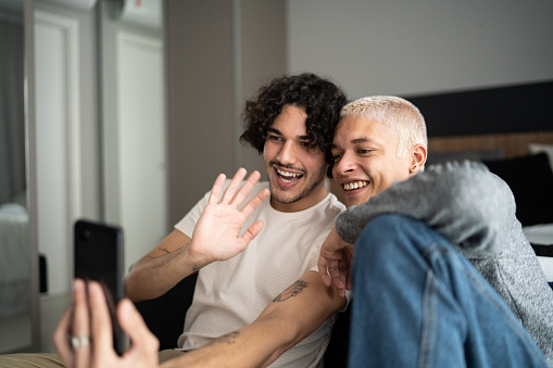 Happy gay couple doing a video call on smartphone at home