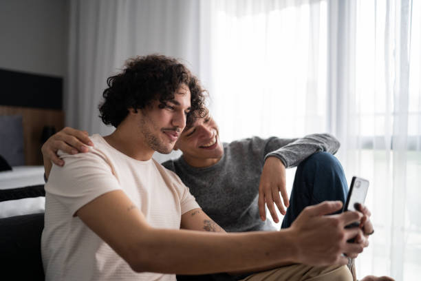 istock Gay couple using mobile phone (doing a video call) at home 1327181958