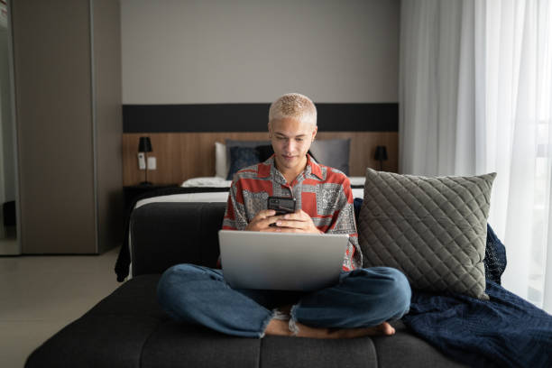 Young man using smartphone and laptop at home Young man using smartphone and laptop at home lgbtqcollection stock pictures, royalty-free photos & images