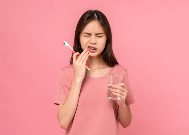 mujer asiática que usa aparatos ortopédicos con dientes cepillados con dientes sensibles y sosteniendo vidrio de agua sobre fondo rosa, concepto de higiene oral y cuidado de la salud. - human face water washing women fotografías e imágenes de stock