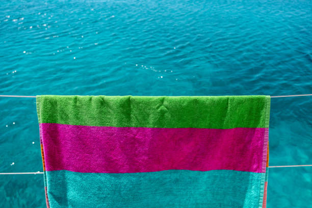 Beach towel drying on clothesline, blur sea background. Colorful towel hanging on boat stainless rail. Summer vacations and sailing, clothes wash and dry. Space, advertise template