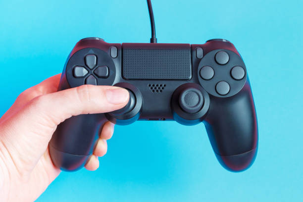 istock Female hand holding video game joystick on blue background close-up. 1327208890