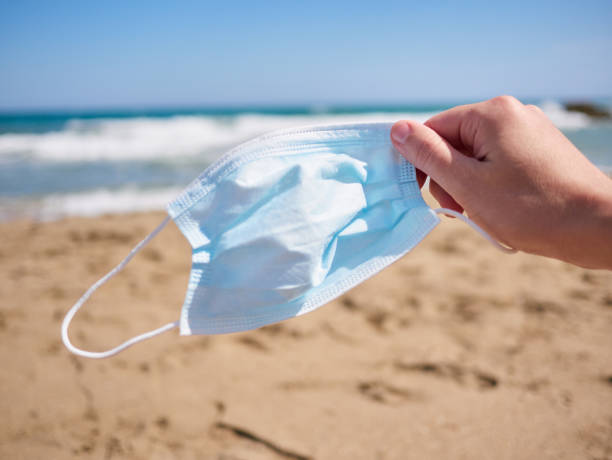 istock Hand holding a face mask on a beach 1327209853