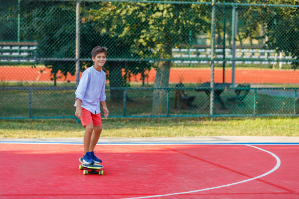 young boy reitet auf einem skateboard in einem öffentlichen park. - skateboard court stock-fotos und bilder