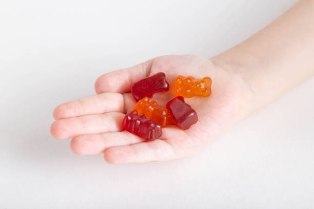 istock Small child's hand holds multicolored kids vitamins teddy bear on white background, isolate. Multivitamins 1327217946