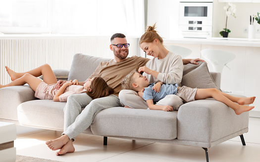 Parents expressing love to kids. Beautiful happy family of four, mother, father and two cute children spending time together at home, embracing and relaxing on sofa in living room