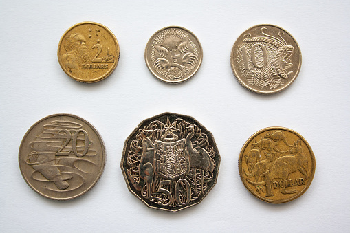 Australian dollar coins arranged in order on a white background. Coins of Australia of different value, from 5 cents to 2 dollars, featuring kangaroos, platypus, emus, lyre bird and Australian Aboriginal.