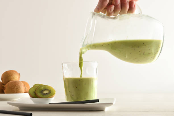 istock Person serving kiwi drink from jug on table isolated white 1327220450