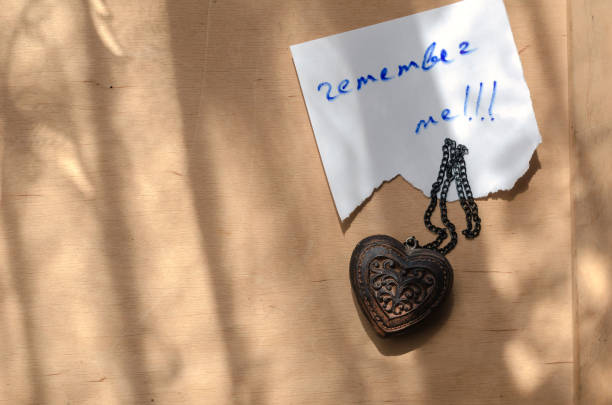 Remember me and the wooden amulet on the yellow surface. A handwritten note on a torn piece of paper. A handmade heart-shaped worn talisman. Love Relationship.