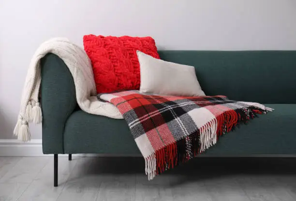 Sofa with soft pillows and warm plaids near light wall indoors