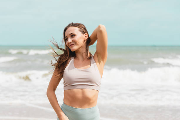 ritratti di atleta allegra in piedi al mare. le donne sportive sane posano per pose sexy e mostrano la loro vestibilità slim del corpo nella giornata estiva. - reggiseno sportivo foto e immagini stock