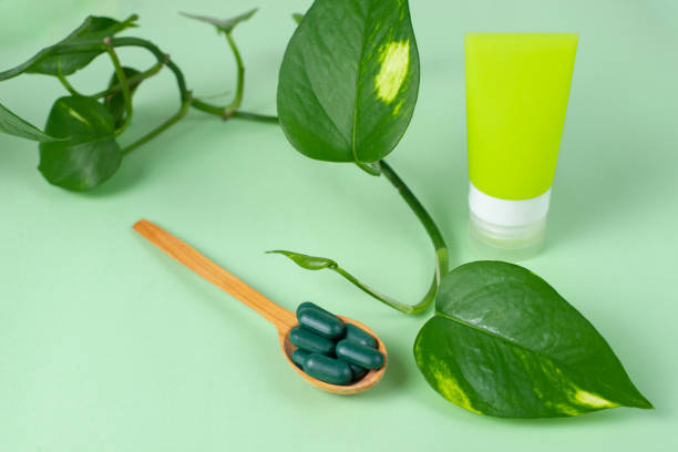 Green capsules for skin, health in wooden spoon near plant leaf on green background. Woman's care, detox program. Natural vitamins pills for youth. Cosmetology and beauty concept. cápsulas verdes para la piel, salud en cuchara de madera cerca de la hoja de la planta sobre fondo verde. cuidado de la mujer, programa de desintoxicación. píldoras de vitaminas naturales para la juventud. concepto de cosmetología y belleza