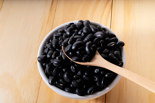 Raw black beans in a wooden spoon and a bowl close up on the table. horizontal view from above