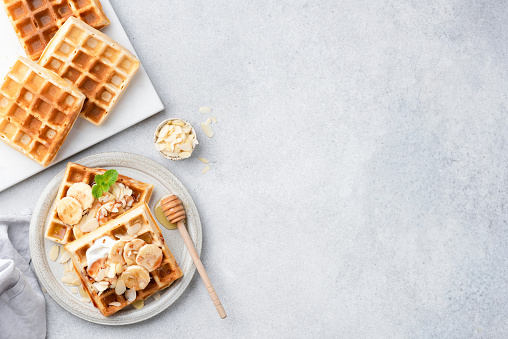 Belgian waffles with banana, caramel and cream on a grey concrete stone background, top view, copy space