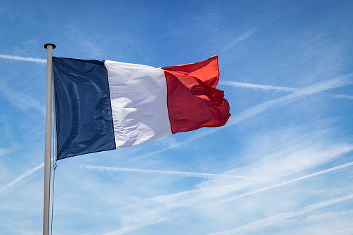 Tricolored striped flag on flag pole against blue sky. Flag of France. 14th July, Bastille Day. Blue, white and red colors, French flag.