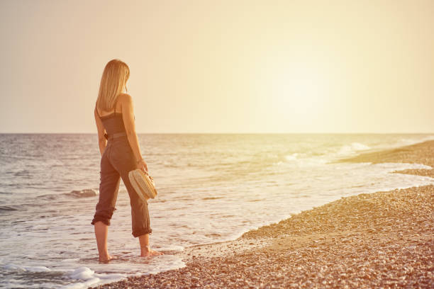 woman with slim body walking on the beach at sunset stock photo
