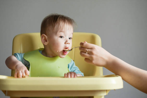 istock little child eats on gray background, mom feeds the baby with a spoon 1327237143