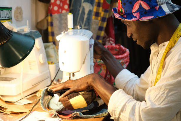 istock African tailor smiling sewing a hat with sewing machine at sewing workshop. Black man working with african fabrics. 1327240853