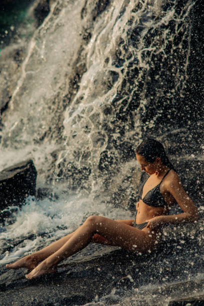 istock Woman sits under the waterfall and enjoys the falling water. 1327241690