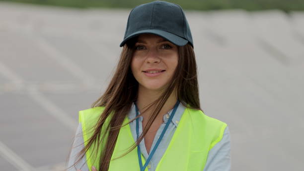 istock Female electrical worker in working clothes smiling while stand at solar power farm. Solar panel field. Clean energy production. Green energy. 1327242010
