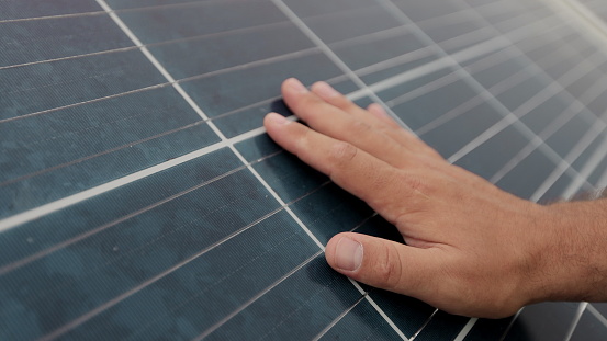 Close up of a young man engineer hand is checking the operation of sun and cleanliness of photovoltaic solar panels. Concept for ecology. Solar farm. Clean energy concept