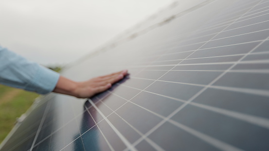 Close up of a young woman engineer hand is checking the operation of sun and cleanliness of photovoltaic solar panels on a sunset. Concept.renewable energy, technology, electricity, service, green