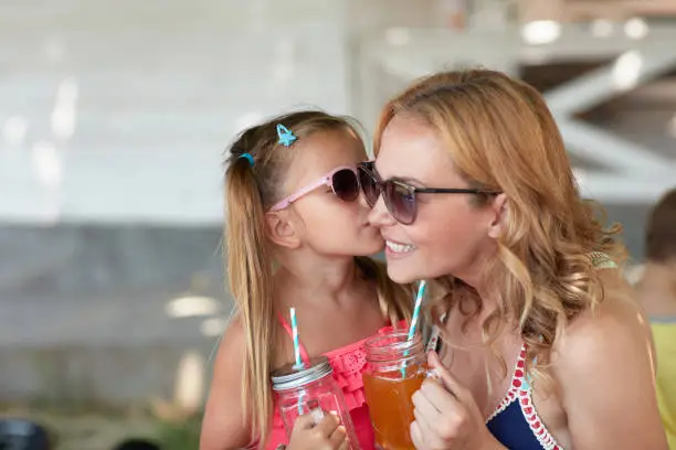 Photo of cute little girl kissing her mom in the cheek