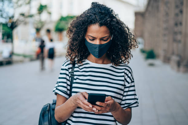 istock Woman with protective mask using smartphone outdoors in the city. 1327248833
