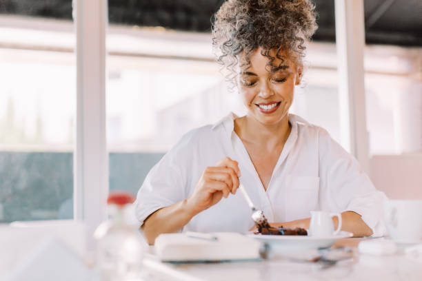 Cheerful mature woman eating some cake in a cafe Cheerful mature woman having some cake in a cafe. Happy mature woman smiling while sitting at a cafe table. Mature woman having lunch alone. lunch break stock pictures, royalty-free photos & images