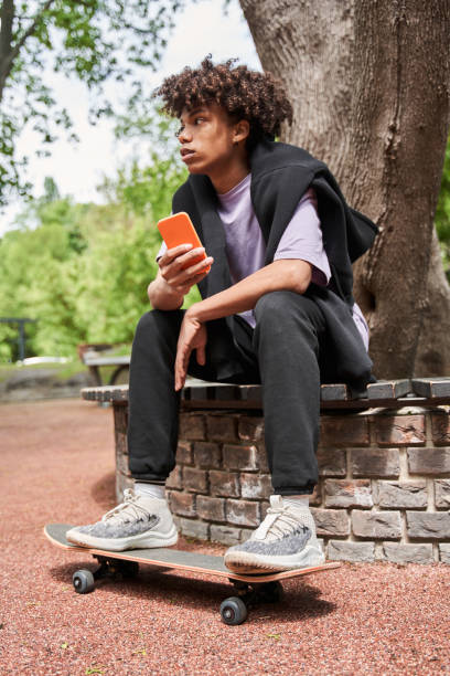 istock Skateboarder sitting at the bench and looking away while using smartphone 1327252223