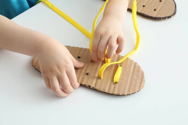 istock Little boy tying shoe lace using training cardboard template at white table, closeup 1327254337