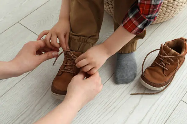 Photo of Mother helping son to tie shoe laces at home, closeup