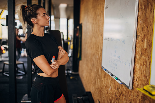 One woman, beautiful fit woman in gym, she is looking at training schedules on whiteboard.