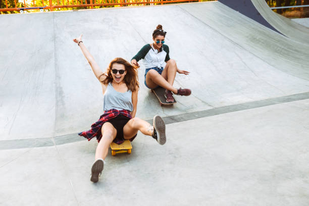 Two cheerful young girls having fun Two cheerful young girls having fun while riding on skateboards at the park skateboard stock pictures, royalty-free photos & images