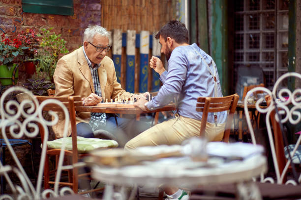 istock young beardy guy playing chess with elderly man, sitting in outdoor cafe 1327256231