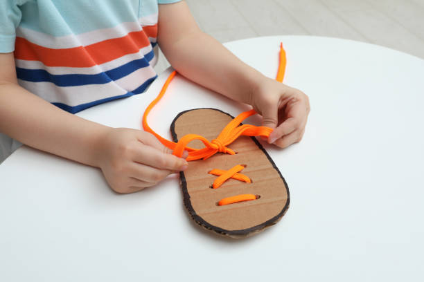 istock Little boy tying shoe lace using training cardboard template at white table, closeup 1327256238