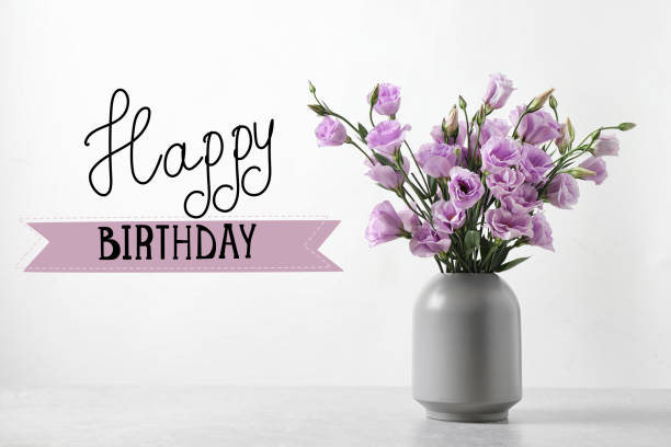 istock Happy Birthday! Eustoma flowers in vase on table near white wall 1327257341