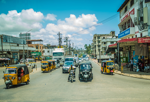 Mombasa, Kenya - September 27, 2016: Mombasa Street with traffic typical for this part of the world - tuk tuk. Neglected, poor buildings, shops and palm trees in the background.