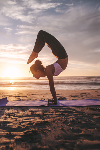 Woman doing yoga asana on the beach at sunset. Fitness female practicing pincha mayurasana scorpion along the sea.