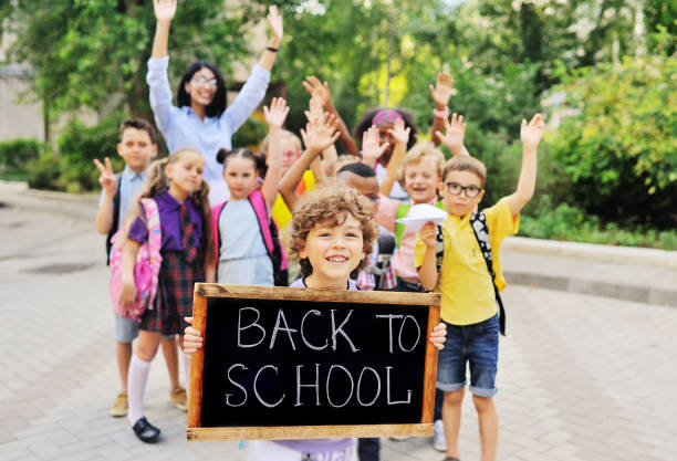 schoolboy with curly hair on the background of a group of children classmates holding a sign with the inscription "back to school stock photo