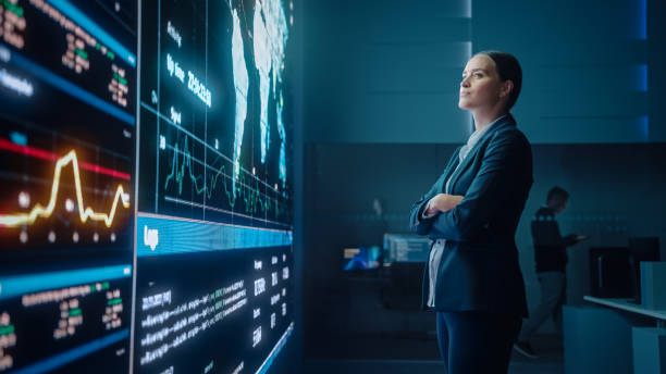 istock Young Female Computer Science Engineer Looking at Big Screen Display Showing Global Map with Data Points. Telecommunications Technology Company System Control and Monitoring Room with Servers. 1327262867