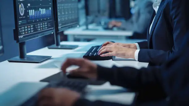 Photo of Close Up Hands Shot of a Technical Support Specialist of Software Engineer Working on a Computer in a Dark Monitoring and Control Room. He types on Keyboard and Moves the Mouse.