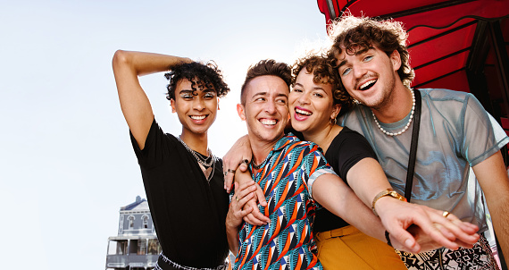 Cheerful group of friends having fun together outdoors. Four young queer people smiling while standing together and embracing each other. Friends bonding and spending time together.