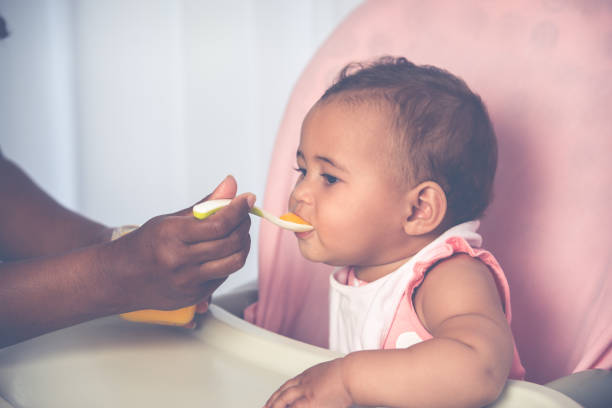 istock Cute baby child eating pureed mango with a teaspoon. 1327264398