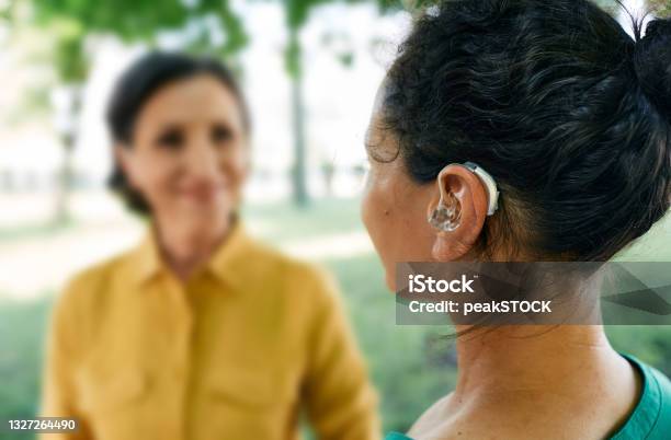 Adult Woman With A Hearing Impairment Uses A Hearing Aid To Communicate With Her Female Friend At City Park Hearing Solutions Stock Photo - Download Image Now