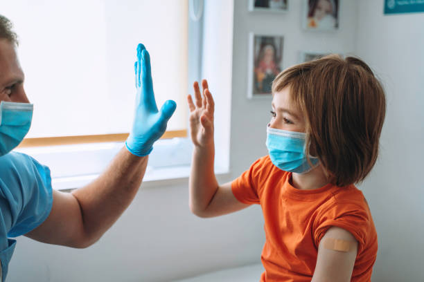 arzt und niedlicher junge geben sich nach covid-19 impfung hochfünf. kinderimpfung. coronavirus-epidemie. kopieren sie den speicherplatz. - nurse high five mask stock-fotos und bilder