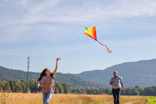 Grandfather and his granddaughter flying a kite outdoors and having fun