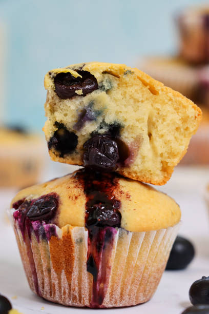 zbliżenie obrazu domowej roboty babeczki jagodowe w papierowych przypadkach ciasto ułożone na siebie, rozpakowane muffin pokroić na pół, w otoczeniu świeżych jagód, jasnoniebieskie tło, skupić się na pierwszym planie - blueberry muffin zdjęcia i obrazy z banku zdjęć